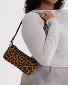 Eine Frau in einem hellgrauen langärmeligen Oberteil und einem Satinrock trägt die BAGGU Nylon Pochette, eine kompakte Crossbody-Tasche mit Leopardenmuster von BAGGU, über der Schulter.