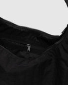 Eine Nahaufnahme einer geöffneten BAGGU Nylon Shoulder Bag von BAGGU zeigt eine Innentasche mit Reißverschluss und einen Hauptreißverschluss vor einem hellen Hintergrund, der das moderne, nachhaltige Design der Tasche unterstreicht.