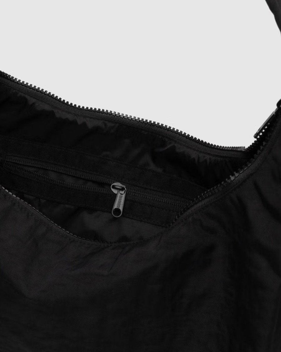 Eine Nahaufnahme einer geöffneten BAGGU Nylon Shoulder Bag von BAGGU zeigt eine Innentasche mit Reißverschluss und einen Hauptreißverschluss vor einem hellen Hintergrund, der das moderne, nachhaltige Design der Tasche unterstreicht.