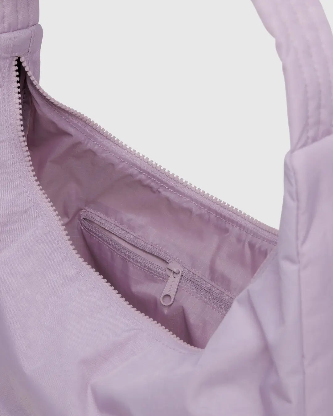 Nahaufnahme der BAGGU Nylon-Umhängetasche in Hellviolett, mit einer Innentasche mit Reißverschluss und einem teilweise geöffneten Hauptreißverschluss, der das Stofffutter sichtbar macht.