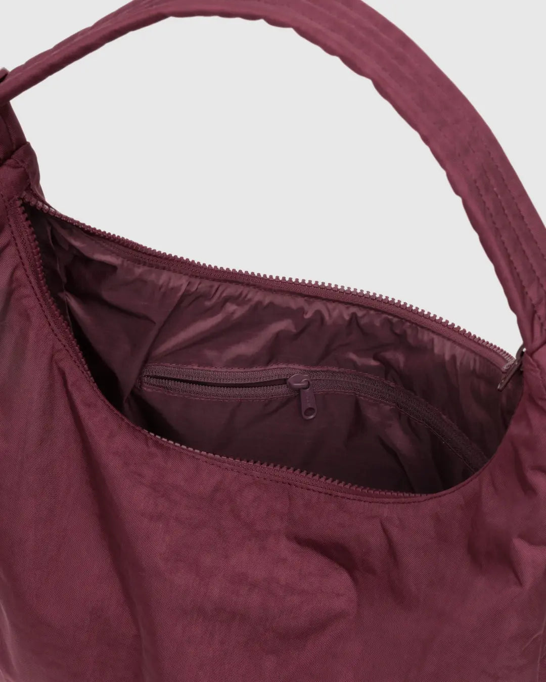 Die Nahaufnahme einer geöffneten BAGGU Nylon-Schultertasche zeigt das Hauptfach, die Innentasche mit Reißverschluss und den stabilen Griff - ideal für alle, die einen nachhaltigen Stil suchen.
