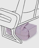 Eine hellviolette BAGGU Small Cloud Carry-On Tasche aus recyceltem Nylon liegt unter einem Stuhl mit schwarzen Konturen, die über das reale Foto der Tasche illustriert sind. Der Hintergrund ist in hellem Grau gehalten.