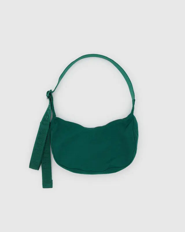 Die BAGGU Small Nylon Crescent Bag von BAGGU ist eine kompakte grüne Umhängetasche mit geschwungener Silhouette, breitem Riemen und Stoffanhänger, hergestellt aus recyceltem Nylon und abgebildet auf einem schlichten hellgrauen Hintergrund.