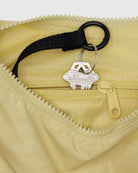 Ein silberner Hausschlüssel an einem schwarzen Schlüsselring ist am Reißverschluss einer kleinen gelben Reißverschlusstasche in einer hellgelben BAGGU Small Nylon Crescent Bag von BAGGU befestigt - eine umweltfreundliche Wahl.