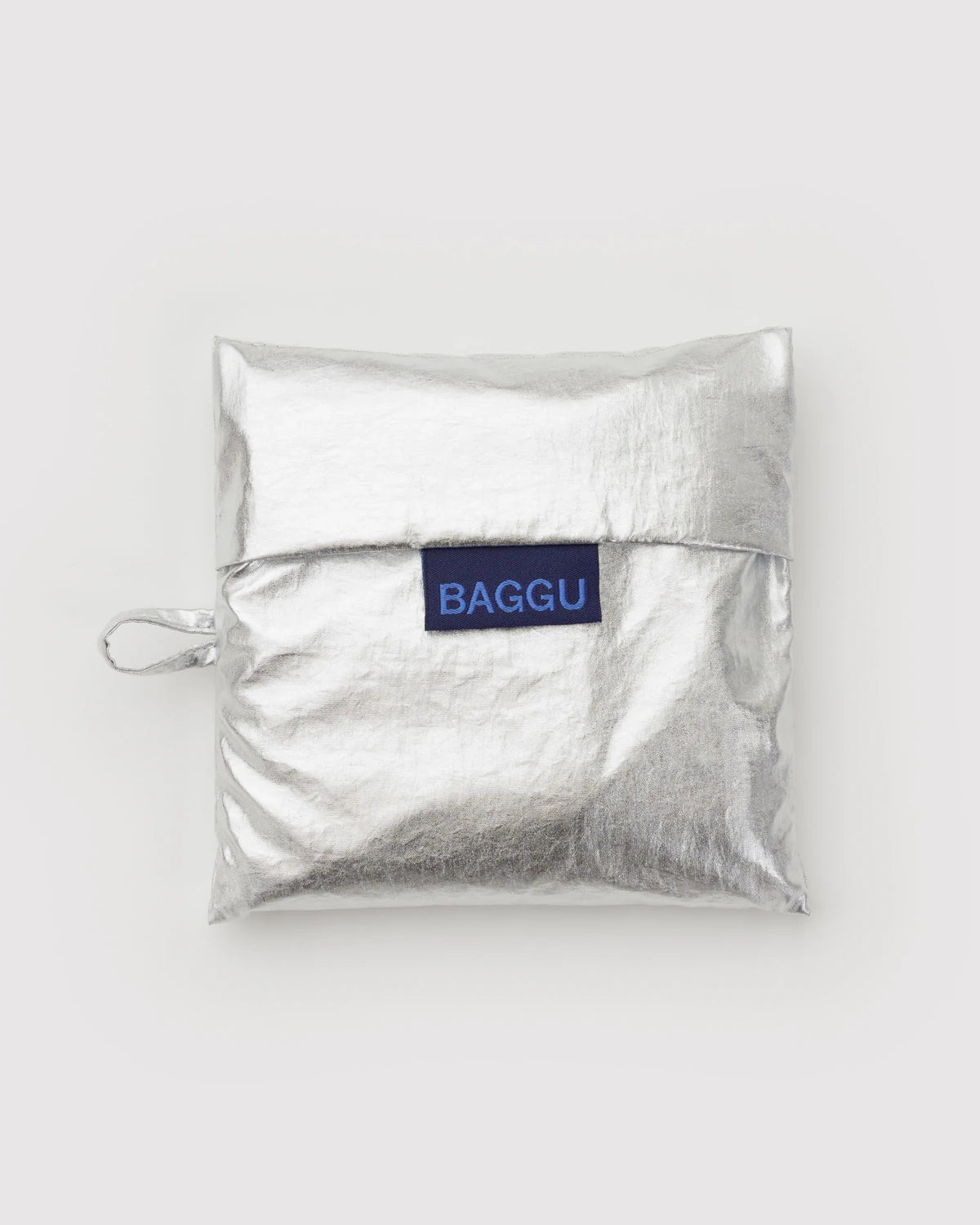Eine quadratische metallic-silberne BAGGU Standard Tragetasche aus recyceltem Ripstop-Nylon mit seitlicher Schlaufe und blauem "BAGGU"-Label, präsentiert vor einem schlichten hellgrauen Hintergrund.