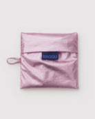 Metallicrosa, quadratische BAGGU Standard Tragetasche aus recyceltem Ripstop-Nylon, gefaltet mit Überschlag und Seitenschlaufe, mit blauem "BAGGU"-Label.