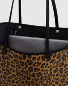 Eine Nahaufnahme einer großen, wendbaren BAGGU-Nylon-Tragetasche im Leopardenmuster mit schwarzen Henkeln, die teilweise geöffnet ist und den Blick auf einen silbernen Laptop im Inneren freigibt.