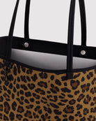 Eine Nahaufnahme einer BAGGU Medium Nylon Reversible Tote mit Leopardenmuster, schwarzen Tragegriffen und silbernen Druckknopfverschlüssen am oberen Rand, die den charakteristischen, zeitlosen Stil der Marke verkörpert.