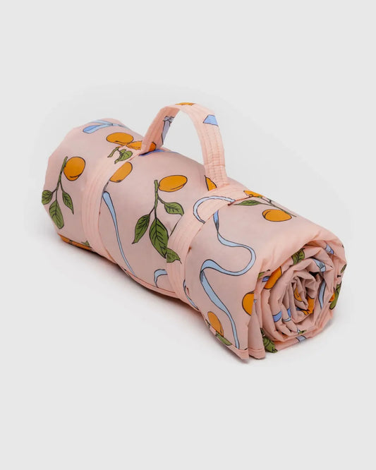 Die bauschige Picknickdecke „BAGGU“ mit Hauptdesign ist eine aufgerollte rosa Nylondecke mit Orangen und Blättern und verfügt über einen Griff zum einfachen Tragen.