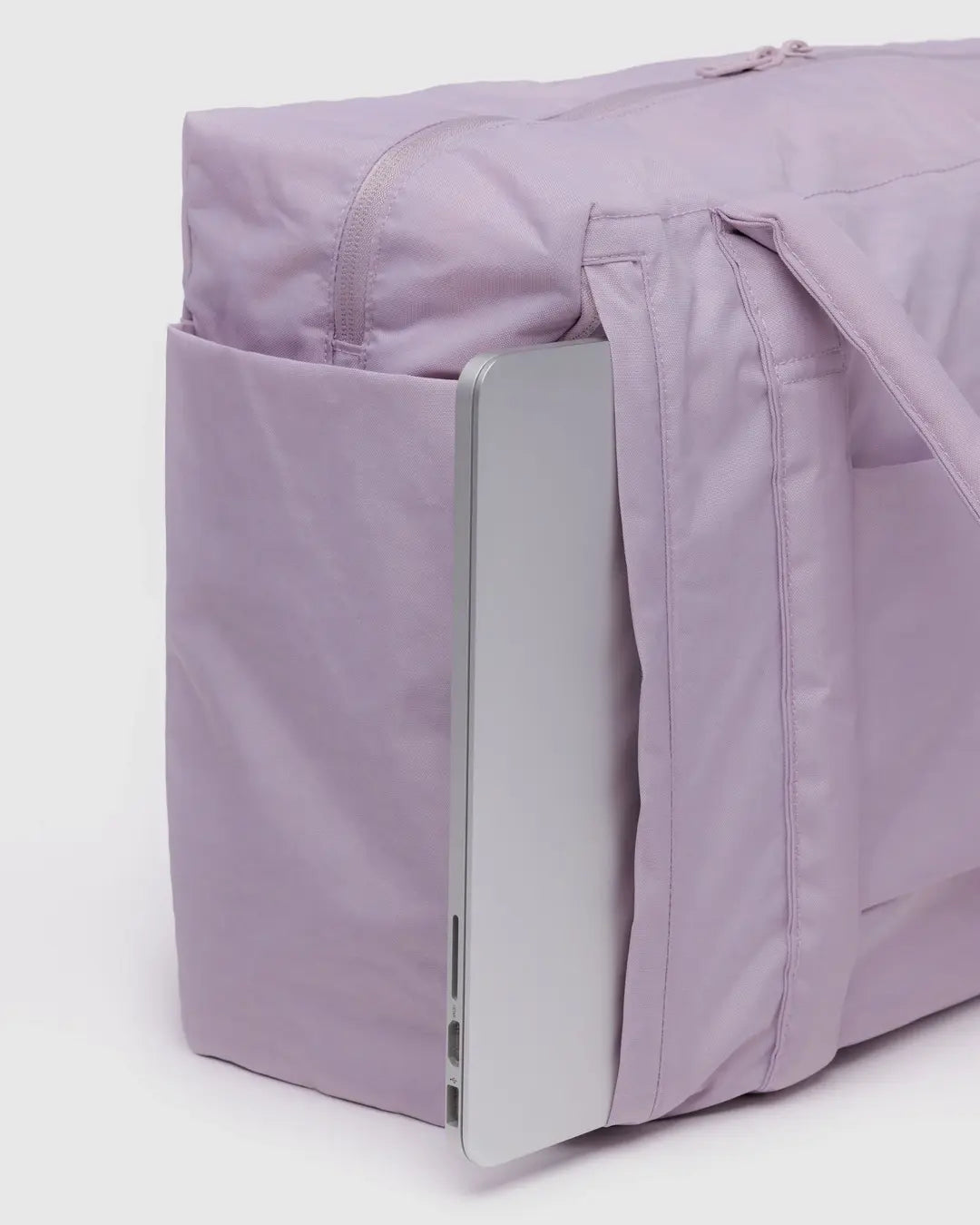 Die BAGGU Small Cloud Carry-On Tasche von Main Design in Lavendel ähnelt einer schicken Tasche, aus deren Seitentasche ein Laptop hervorschaut. Sie verfügt über Griffe und einen Reißverschluss oben und hebt sich stilvoll von einem schlichten Hintergrund ab.