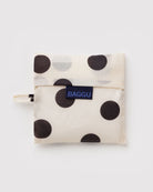 Die BAGGU Standard Tragetasche ist eine zusammenfaltbare, wiederverwendbare Tasche aus recyceltem Ripstop-Nylon mit großen schwarzen Punkten, die in einem passenden Beutel verpackt ist und auf der Vorderseite mit einem blauen BAGGU-Etikett versehen ist.
