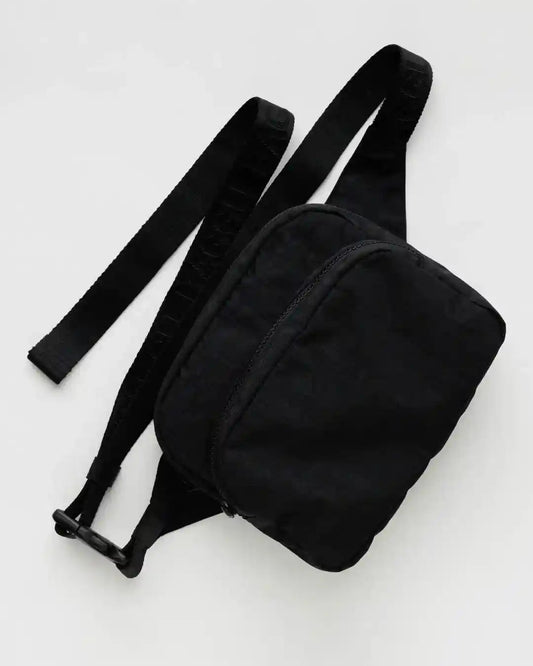 Eine kleine schwarze BAGGU-Gürteltasche von Main Design mit verstellbarem Riemen liegt auf einer hellgrauen Oberfläche. Diese Nylontasche verfügt über einen Reißverschluss und ein kompaktes Design, ideal zum Tragen wichtiger Dinge.