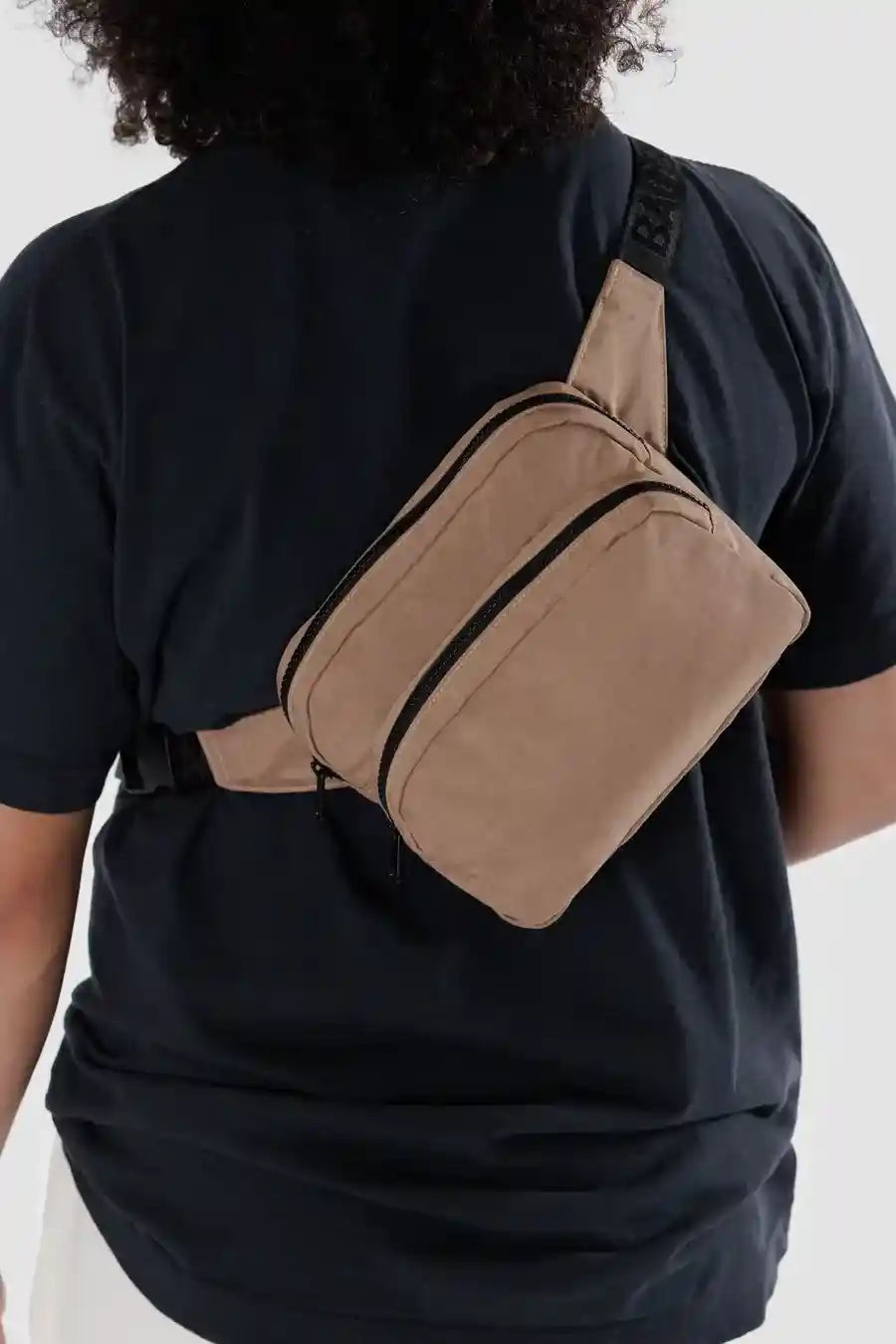 Eine Person trägt ein schwarzes T-Shirt mit einer stylischen BAGGU-Gürteltasche von Main Design aus recyceltem Nylon mit zwei Fächern mit Reißverschluss, die über ihren Rücken hängt.