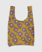 Die BAGGU Standard Tragetasche von Main Design hat einen gelben Hintergrund mit großen lila Blumen und grünen Stielen. Hergestellt aus recyceltem Ripstop-Nylon, hat diese wiederverwendbare Tasche breite Henkel und eine robuste, rechteckige Form.