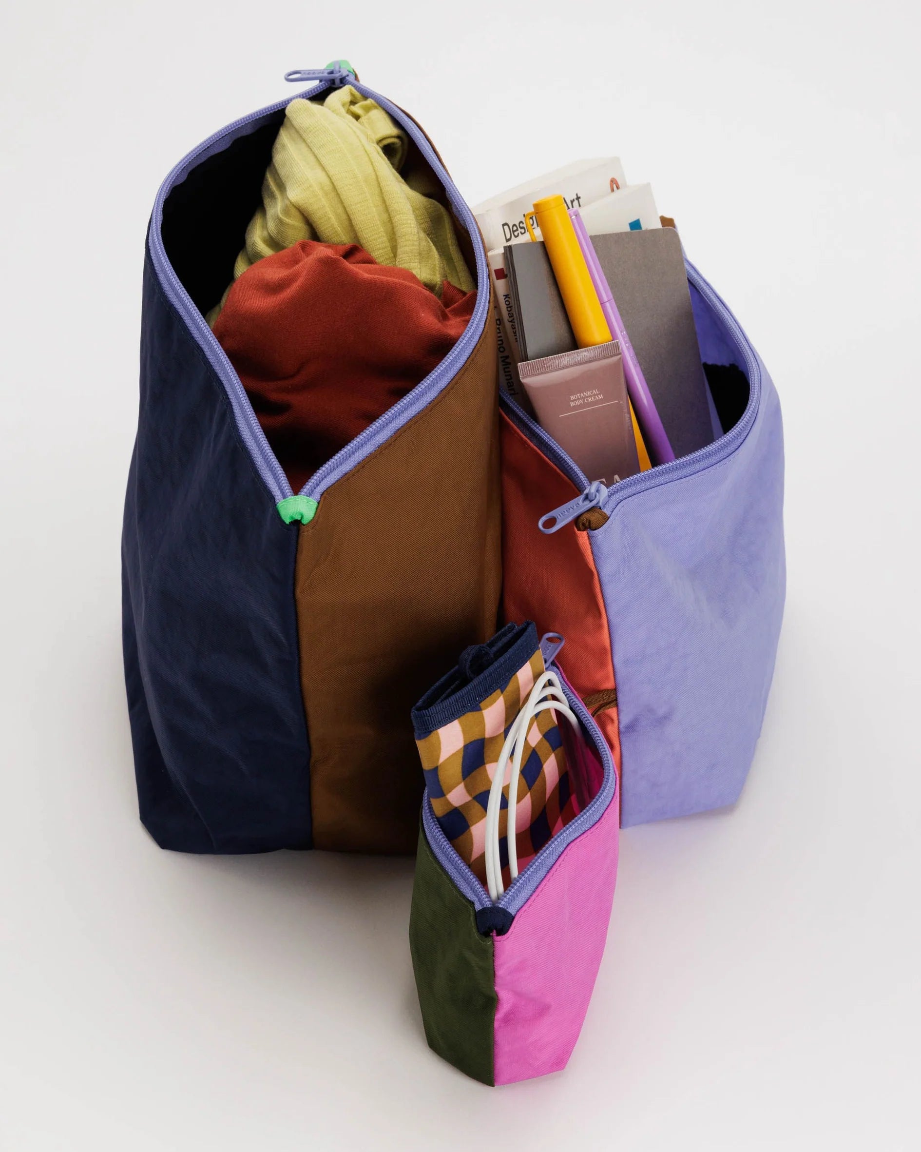 Drei farbenfrohe Stofftaschen mit Reißverschluss in unterschiedlichen Größen sind vor einem schlichten Hintergrund zu sehen. Das Main Design BAGGU Go Pouch Set aus recyceltem Nylon bietet Platz für verschiedene Gegenstände, darunter Kleidung, Bücher, einen gelben Bleistift und ein kariertes Federmäppchen – eine ideale Wahl für umweltbewusste Taschenliebhaber.