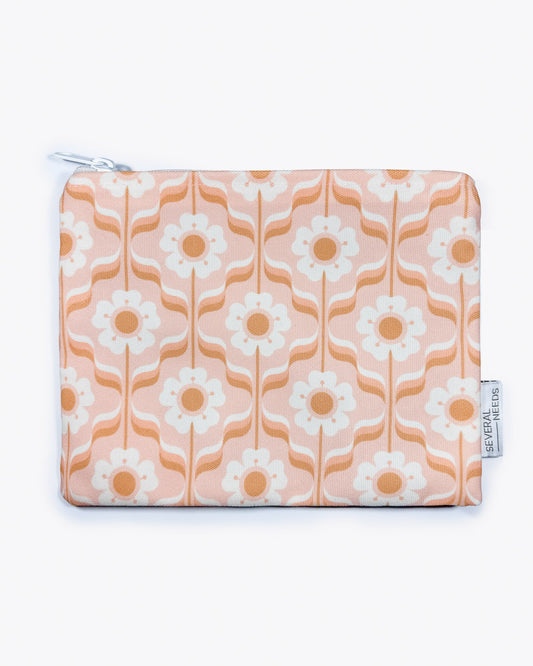Die Bikini Tasche von Several Needs by Main Design ist eine handgefertigte, rechteckige Tasche mit wasserabweisendem Design. Sie besteht aus stilisierten weißen Blumen mit orangefarbenen Blüten auf pfirsichfarbenem Hintergrund, vertikalen Wellenlinien und einem weißen Reißverschluss. An der Seite befindet sich ein kleines Etikett.