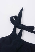 Eine Nahaufnahme des Main Design Mia Mädchen Bikinis, aus dunkelmarineblauem Stoff mit strukturierter Oberfläche. Das Bikinioberteil aus recycelten Materialien zeigt sein elegantes Neckholder-Design mit einem ordentlich gebundenen Knoten an einer Ecke. Der schlichte weiße Hintergrund hebt die komplizierten Details dieses Kleidungsstücks hervor.