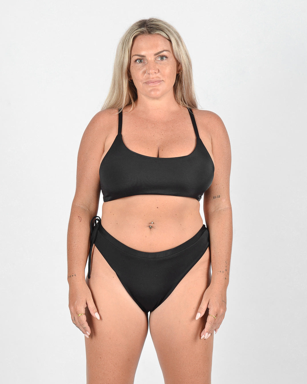 Eine Frau mit langen blonden Haaren trägt eine Blush Surf Bikinihose von Main Design aus umweltfreundlichem Stoff. Sie steht mit neutralem Gesichtsausdruck und entspannten Armen vor einem schlichten weißen Hintergrund und blickt in die Kamera.
