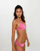 Eine Frau mit langem, dunklem Haar steht vor einem hellen Hintergrund. Sie trägt das Main Design Pasta Bikini Oberteil mit seitlich gebundener Hose aus recycelten Materialien und blickt mit neutralem Gesichtsausdruck direkt in die Kamera.