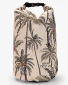 Eine beige wasserdichte Dry Bag von Meraki Supply Co. von Main Design, verziert mit einer Illustration von Palmen mit grünen Blättern und braunen Stämmen. Die Tasche hat einen schwarzen Schnallenverschluss an der Oberseite und den Text „MERAKI SUPPLY CO.“ in der unteren rechten Ecke, was sie perfekt für die Aufbewahrung Ihrer Reiseutensilien macht.