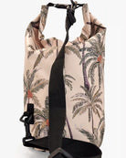 Der Dry Bag von Meraki Supply Co. by Main Design zeigt einen tropischen Palmendruck auf beigem Hintergrund. Er ist mit einem schwarzen verstellbaren Schultergurt, einem stabilen Schnallenverschluss an der Oberseite und einem gerollten Design zum Sichern und Verschließen Ihrer Reiseutensilien ausgestattet.