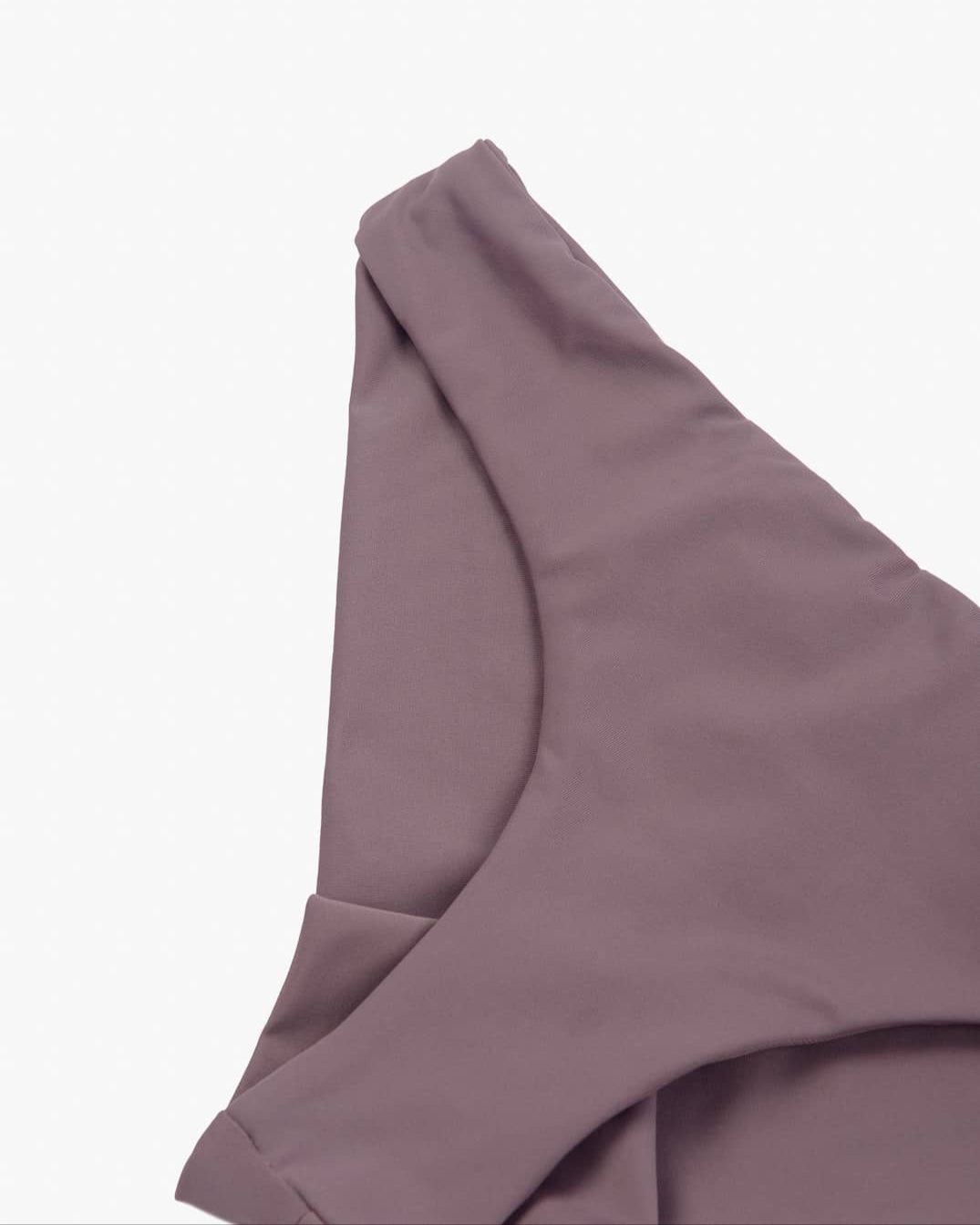 Nahaufnahme eines malvenfarbenen Stoffes, der in weichen Falten drapiert ist und teilweise eine nahtlose Verarbeitung aufweist. Das Material wirkt leicht und hat einen subtilen Glanz, was darauf hindeutet, dass es aus recycelten Materialien hergestellt sein könnte. Dies ist die Dusk Bikinihose von Main Design.