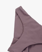 Nahaufnahme eines malvenfarbenen Stoffes, der in weichen Falten drapiert ist und teilweise eine nahtlose Verarbeitung aufweist. Das Material wirkt leicht und hat einen subtilen Glanz, was darauf hindeutet, dass es aus recycelten Materialien hergestellt sein könnte. Dies ist die Dusk Bikinihose von Main Design.