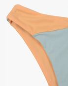 Nahaufnahme der Flair Bikinihose von Main Design aus der Cali Coast Collection mit pfirsichfarbenem Bund und himmelblauem Stoff. Der leicht gedrehte Bund verstärkt den Kontrast des Colorblock-Stils und sorgt für einen lässigen und entspannten Look.