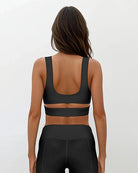 Eine Frau mit langen braunen Haaren blickt in die Ferne. Sie trägt das Main Design Flow Active Top mit einem breiten horizontalen Träger und dazu passende Leggings mit hoher Taille vor einem schlichten hellen Hintergrund.