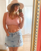 Eine Frau in einem hellen Raum mit Holzfußboden macht ein Selfie im Spiegel. Sie trägt das Main Design Hale Bikini Oberteil und einen leichten Jeansrock mit Vogelmotiven, dazu einen breitkrempigen Hut.