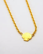 Die Halskette von Adorabili ist eine zarte 24K vergoldete Goldkette mit einem fein gravierten Muschelanhänger, der auf einem schlichten weißen Hintergrund abgebildet ist. Ideal als Geschenk für Kinder.