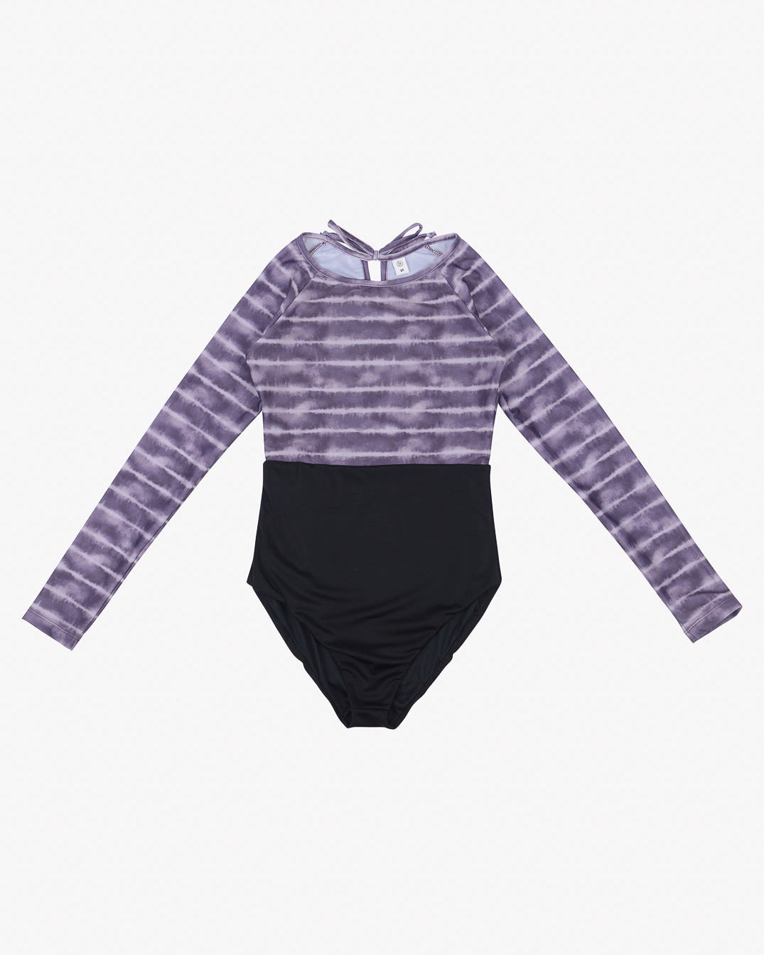 Ein langärmliger Ivy Surf Suit von Main Design mit einem lila-weißen Batikmuster auf der oberen Hälfte und einer schwarzen unteren Hälfte. Der Ivy Surf Suit aus recycelten Materialien hat einen runden Ausschnitt und ein Schlüsselloch-Detail auf der Rückseite mit einer kleinen Schleife oben. Dieses moderne und stilvolle Design bietet LSF 50+-Schutz.