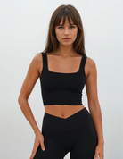 Eine Frau mit langen braunen Haaren und Pony trägt ein schwarzes, tailliertes Crop-Top und die Juno Leggings von Main Design, die eine hohe Taille hat und aus recyceltem Nylon hergestellt ist, während sie vor einem schlichten, hellen Hintergrund steht.