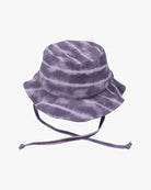 Ein lilafarbener **Kinder-Sonnenhut** mit Batikmuster, breiter Krempe und verstellbaren Kinnriemen, hergestellt aus umweltfreundlichem Stoff. Der Hut weist ein Muster aus horizontalen Streifen in verschiedenen Lila- und Weißtönen auf und bietet hervorragenden Sonnenschutz (LSF 50+). Er ist von **Main Design**.