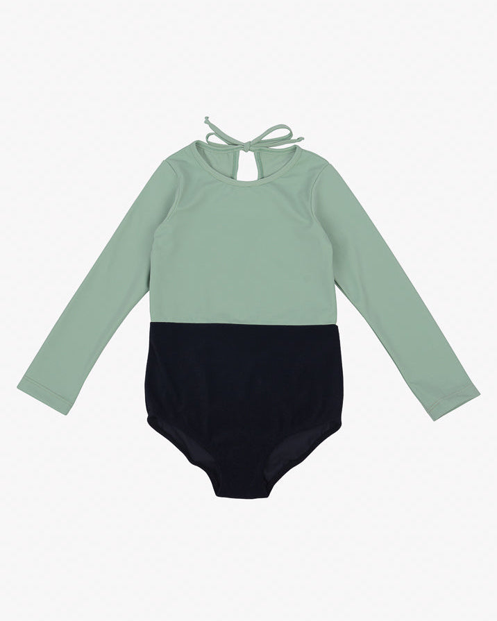 Der Laila Mädchen Badeanzug von Main Design ist ein langärmliger, zweifarbiger Badeanzug mit mintgrünem Oberteil und schwarzem Unterteil. Er hat einen schlüssellochförmigen Ausschnitt auf der Rückseite mit einem Bindeverschluss am Hals. Dieses elegante Design aus umweltfreundlichem Stoff mit LSF 50+ Sonnenschutz ist perfekt für Kinder.