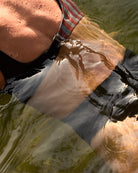 Im Badeanzug Luna von Main Design aus recycelten Materialien mit seitlichen Aussparungen ist eine Person teilweise in grünliches Wasser getaucht, während sich das Sonnenlicht auf ihrer Haut und der Oberfläche spiegelt.