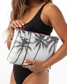 Eine Frau in einem schwarzen Badeanzug hält die geräumige „Aloha Mid Pouch“ von Aloha Collection in der Hand, die mit auffälligen schwarzen Palmenmotiven verziert ist. Dieses vielseitige Accessoire eignet sich sowohl als schicke Kosmetiktasche als auch als praktischer Reise-Organizer und ist damit die ideale Wahl für stilvolles Reisen. Der schlichte weiße Hintergrund lenkt die Aufmerksamkeit sowohl auf die Tasche als auch auf ihr Outfit und unterstreicht den mühelosen Reise-Chic.