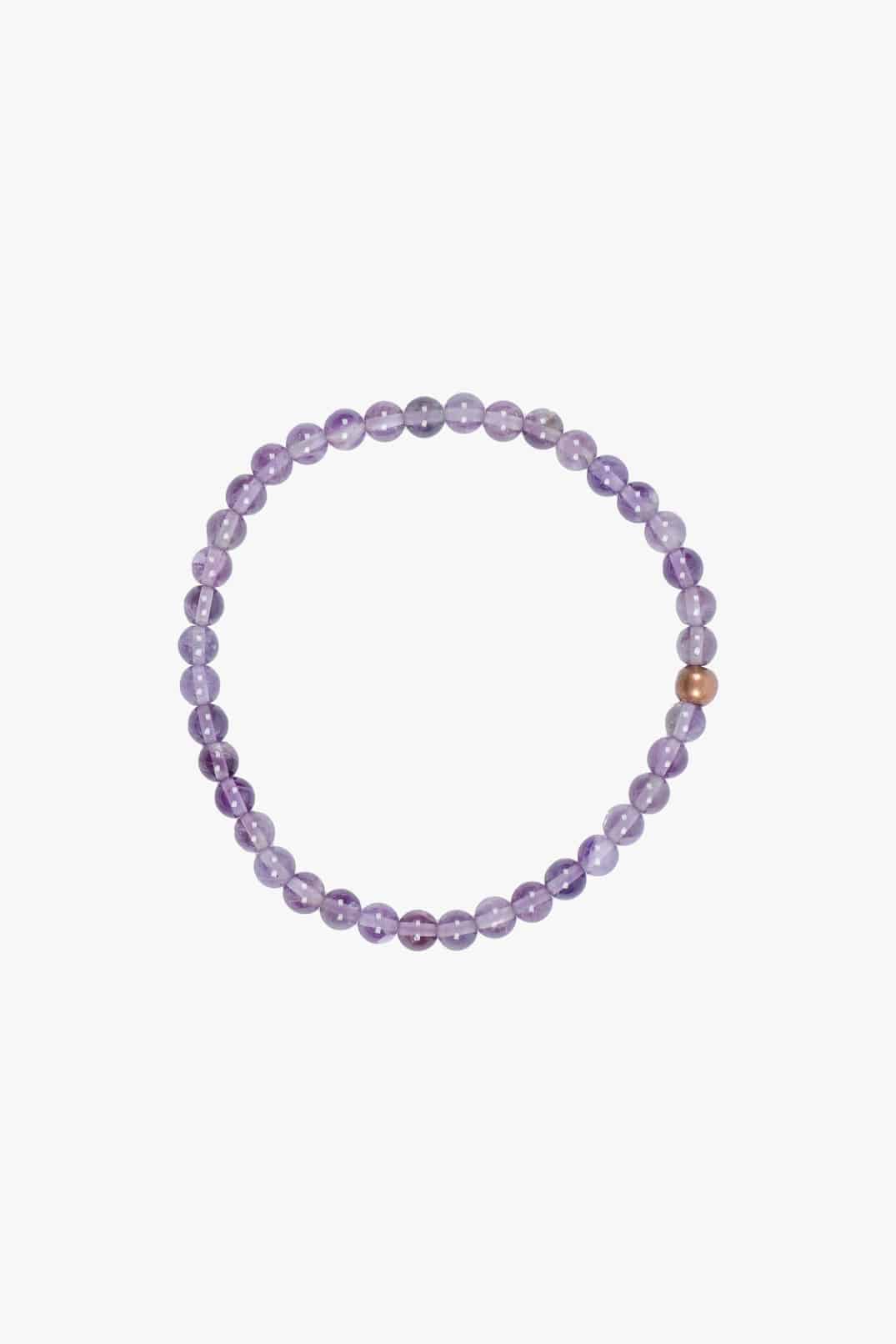 Ein Perlenarmband aus runden, halbtransparenten Amethyststeinen mit einer einzelnen kontrastierenden Kupferperle. Die Perlen sind gleichmäßig auf einem elastischen Faden angeordnet und bilden eine kreisförmige Form. Diese Mini und Mama Edelsteinarmbänder von Main Design sind vor einem schlichten weißen Hintergrund zu sehen.