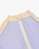 Nahaufnahme der Rückseite des Kai Baby Badeanzugs von Main Design mit weißem Reißverschluss. Der aus nachhaltigen Materialien gefertigte Stoff ist hauptsächlich hellviolett mit hellgelben Akzenten an den Nähten und am Kragen. Der Reißverschluss verläuft vertikal vom Kragen nach unten.