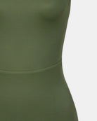 Nahaufnahme einer Person, die den taillierten, olivgrünen Divine Surf Badeanzug von Main Design trägt, der aus recycelten Materialien hergestellt wird. Der glatte, leicht dehnbare Stoff ist am Oberkörper vor einem einfarbig weißen Hintergrund zu sehen.