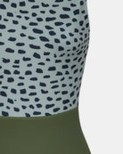 Nahaufnahme des Divine Surf Badeanzugs von Main Design: ein ärmelloser, nachhaltiger Badeanzug aus recycelten Materialien mit einem unregelmäßigen Punktmuster in Marineblau auf Hellgrau im Oberteil und unifarbenem Olivgrün im Unterteil.