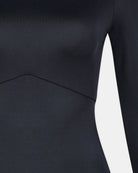 Nahaufnahme des Main Design Eclipse Surf Suit, ein schwarzer, taillierter Anzug aus nachhaltigem Material, der den Torso und einen langen Ärmel mit einer sichtbaren diagonalen Naht über der Taille vor einem weißen Hintergrund hervorhebt.