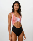 Eine Frau präsentiert vor einem schlichten hellen Hintergrund den Main Design Nova Badeanzug, einen einteiligen Badeanzug mit roten und weißen Streifen oben, einfarbig schwarz unten und einem großen Ausschnitt in der Taille aus recycelten Materialien.