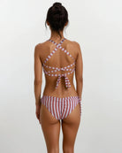 Eine Frau mit hochgestecktem Haar steht mit dem Rücken zur Kamera. Sie trägt die Main Design Blush Surf Bikinihose aus chlorresistentem Stoff mit überkreuzten Trägern und einer Schleife am Rücken. Der Hintergrund ist hell und schlicht.