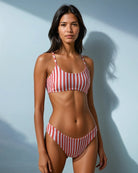 Vor einem hellblauen Hintergrund trägt eine Frau das Sassy Bikini Oberteil reversibel von Main Design aus nachhaltigen Materialien in rot-weiß gestreift und blickt ruhig in die Kamera.
