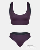 Ein dunkelviolettes Bikini-Set mit einem wendbaren Hale Bikini Oberteil mit Rundhalsausschnitt von Main Design und einem hoch taillierten Unterteil auf einem einfarbig weißen Hintergrund. Der Text in der Ecke lautet: "Besser zusammen, Hale Oberteil | Luxe Unterteil.