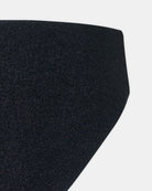 Nahaufnahme der Luxe Glitter Bikini Hose von Main Design: schwarzer Stoff mit glattem, leichtem Glanz, diagonal geschnitten auf einfarbig weißem Grund. Das Material deutet auf hochwertige, umweltfreundliche Bademode aus recycelten Fasern hin.