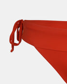 Nahaufnahme der Main Design Serene Surf Bikini Hose in Rot mit seitlichen Bindebändern, hergestellt aus recycelten, chlorresistenten Materialien, dargestellt vor einem einfarbig weißen Hintergrund.
