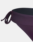 Nahaufnahme der Serene Surf Bikini Hose von Main Design in dunklem Lila, mit seitlichem Bindeband und aus recycelten Materialien gefertigt, vor einem schlichten weißen Hintergrund.