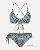 Zweiteiliges Bikini-Set von Main Design aus recycelten Materialien mit weißem Grundton und schwarzen unregelmäßigen Flecken. Das Oberteil hat überkreuzte Träger und einen Binder auf der Vorderseite; die Serene Surf Bikini Hose hat seitliche Bänder.